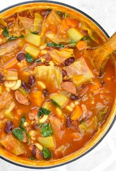 a pot filled with stew and vegetables on top of a table next to a wooden spoon