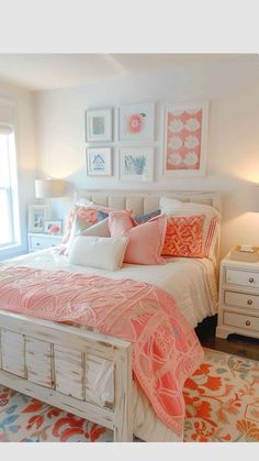 a white bed topped with lots of pillows next to a window covered in pink and orange