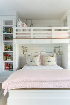 a white bunk bed with pink pillows in a room that has built - in bookshelves