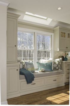 a window seat in the corner of a kitchen with white cabinets and pillows on it