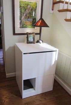 a white cabinet with a lamp on top in front of a staircase case and framed painting