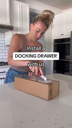 a woman standing in a kitchen with a box on top of it and the words install a docking drawer with us