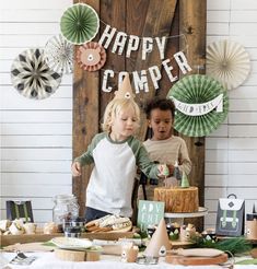 two young children standing in front of a table with cake and decorations on top of it