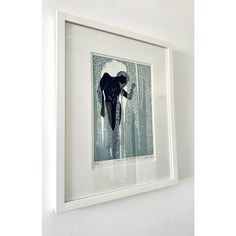 a painting hanging on the wall above a white framed artwork piece with an elephant in it's mouth