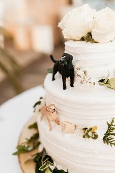 a wedding cake decorated with white flowers and black dog figurines on top is shown