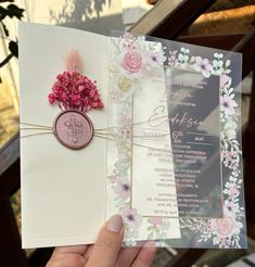 a person holding up a wedding card with flowers on the front and back, in their left hand