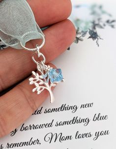 a hand holding a silver tree charm with blue topazte and leaves on it