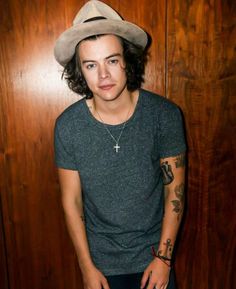 a young man wearing a hat standing in front of a wooden wall with his hands on his hips