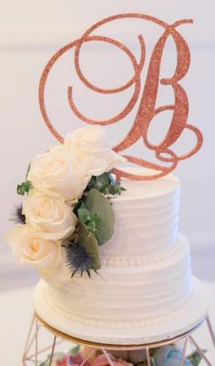 a wedding cake with white flowers and a monogrammed topper on the side