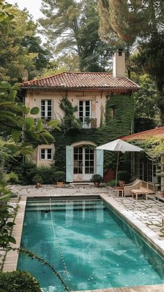 an outdoor swimming pool surrounded by greenery and a house with a patio area next to it