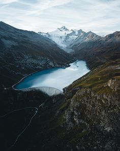 an aerial view of a mountain lake surrounded by snow capped mountains in the distance, with a road running through it