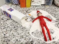 an elf laying on top of a snow covered counter next to a box of milk