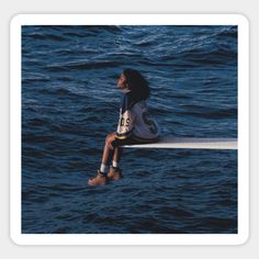 a woman sitting on the edge of a boat in the ocean looking up at the sky