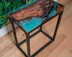 a wooden table with blue paint on it sitting in front of a green and brown painting