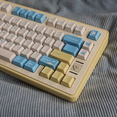 a computer keyboard sitting on top of a blue and yellow blanket covered bedding in front of a window