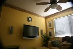 a living room with yellow walls and a ceiling fan in the corner next to a flat screen tv