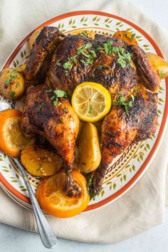 a roasted chicken with lemons and potatoes on a plate next to a fork, knife and napkin