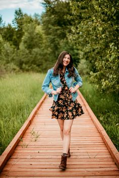 a woman standing on a wooden walkway in the middle of some tall grass and trees