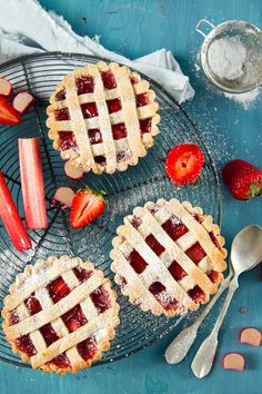 two strawberry pies on a cooling rack with strawberries and rhubarts