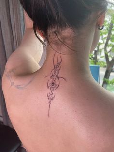 the back of a woman's neck with a tattoo on her left shoulder and an antelope