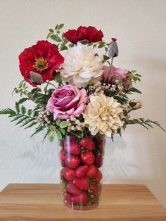 a vase filled with lots of flowers and fruit on top of a wooden table next to a white wall