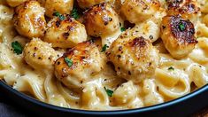 pasta with chicken and cheese in a black bowl on top of a wooden table, ready to be eaten