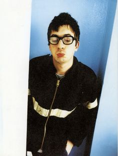 a young man wearing glasses is leaning against a wall