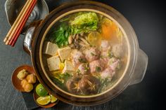 a bowl filled with soup next to chopsticks and other food on a table