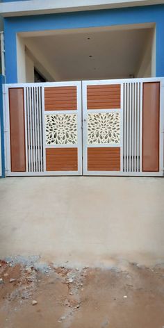 an open gate in front of a blue building with white and brown doors on each side