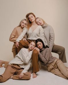 four women are posing for a photo in front of a white background, with one woman sitting on the floor