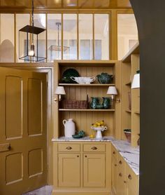 a kitchen with yellow cabinets and marble counter tops in an archway leading to the dining room