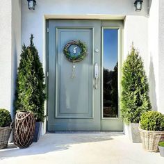 a clock on the front door of a white house with potted plants and baskets