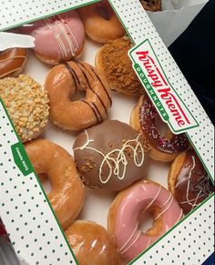 an open box of assorted donuts with frosting and sprinkles