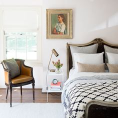 a bedroom with a bed, chair and painting hanging on the wall next to it