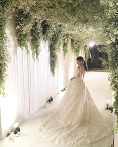 a woman in a wedding dress is standing under an archway covered with flowers and greenery