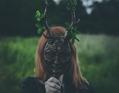 a woman with deer horns and antlers on her head is holding a stick in front of her face