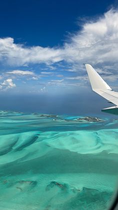 the wing of an airplane flying over water and land with blue skies in the background