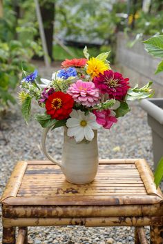 a vase filled with colorful flowers sitting on top of a wooden table next to a potted plant