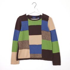 a sweater hanging on a hanger with a white wall in the background and a green, brown, blue, and black checkered pattern