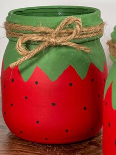 two red and green painted jars sitting on top of a wooden table next to each other