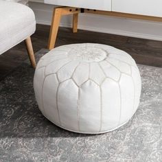 a white ottoman sitting on top of a wooden floor next to a chair and table