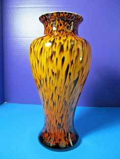 an orange and black vase sitting on top of a blue table next to a purple wall