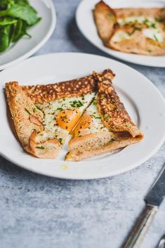 two slices of pizza on a white plate next to some salad and silver utensils