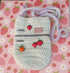 a crocheted purse with strawberries on the front and side, sitting on a pink surface