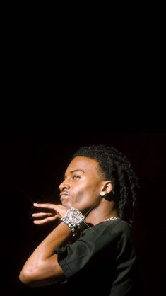 a man with dreadlocks standing in front of a black background holding his hand out