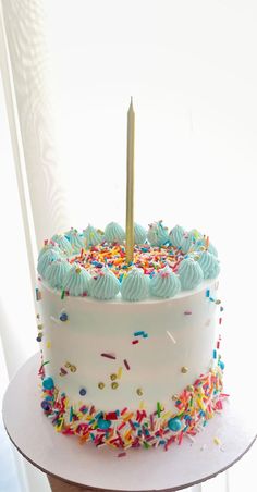 a white cake with sprinkles and a single candle on top is sitting on a table