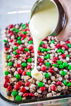 someone is pouring white sauce on some food in a glass pan filled with cereal and m & m