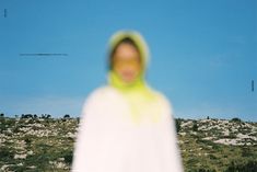 a blurry photo of a woman in a white dress and yellow hoodie standing on a hill