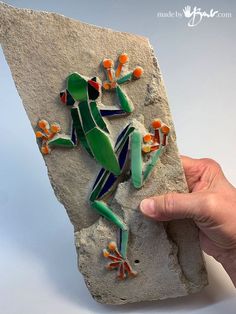 a hand holding up a piece of art that looks like a frog on a rock