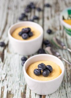 two white bowls filled with blueberries on top of a wooden table next to yogurt